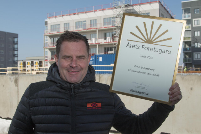 Fredrik visar upp diplomet, i bakgrunden ett av husen han bygger på Gävle Strand